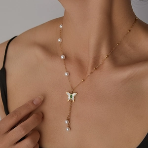 Detailed view of a gold butterfly necklace with green gemstone and pearl tassels on a model