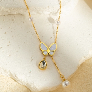 Close-up of golden butterfly pendant with blue inlay and teardrop crystal on pearl chain