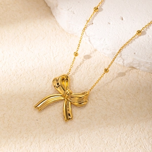 Elegant gold bow pendant necklace with beaded cross chain displayed on natural stone