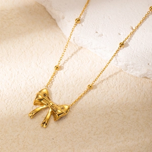 Elegant gold titanium steel bowknot necklace with bead chain on white stone display