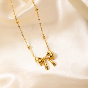 Detailed close-up of a 3D gold ribbon bow pendant with beaded chain on soft satin