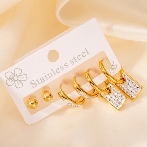 Détail de trois paires de boucles d'oreilles en acier doré et zircons sur tissu satiné