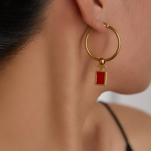 Nahaufnahme eines goldenen Creolen-Ohrrings mit rotem Parfümflaschen-Anhänger am Model