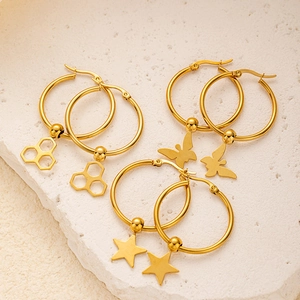 Goldene Creolen-Set mit Schmetterlings-, Stern- und Wabenanhängern auf Stein-Hintergrund