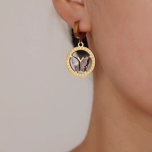 Close-up of 18K gold-plated hoop earrings with dark butterfly pendants worn by a model