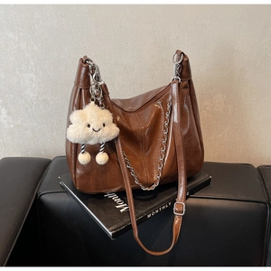 Detail of dark brown leather tote with silver metal chain and plush cloud charm