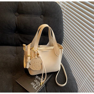 Detail of cream bucket bag with lychee texture, golden zipper, and dog charm on black sofa