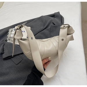 Close-up of beige quilted croissant bag featuring metal eyelet strap detail and pleats