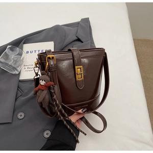Dettaglio della borsa a secchiello marrone scuro con chiusura dorata e ciondolo a orsetto