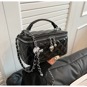 Close-up of quilted black box bag with metallic heart charm and chain strap