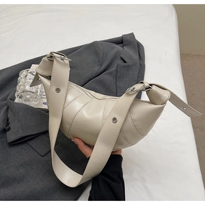 Close-up of beige croissant bag with segment stitching and metallic strap eyelet