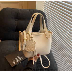 Detail of off-white lychee grain leather bucket bag with a cute puppy charm on chair