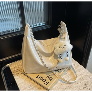 Detail of cream hobo bag with silver chain, long strap and plush cloud charm on marble