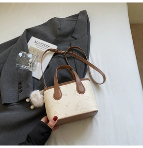 Detail of embossed beige bucket bag with cartoon patterns, brown handle and fur pompom