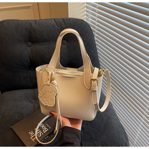 Close-up of beige lychee pattern bucket bag with dog charm and gold-tone hardware