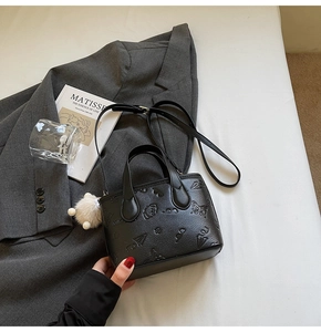 Detail of black embossed handbag with cute patterns and white plush ball charm