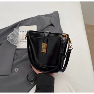 Dettaglio di una borsa a secchiello nera lucida con fibbia dorata e scritta Fashion & Bags
