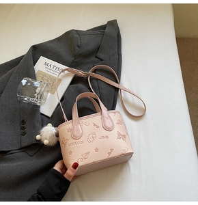Detailed view of pink crossbody bag with embossed cartoon patterns and plush charm accessory