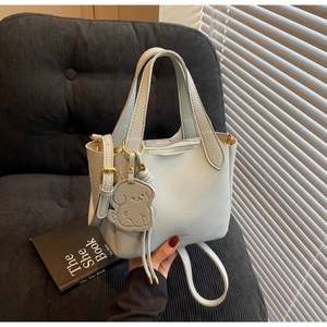 Detail of light blue bucket bag with litchi texture, dog charm and adjustable strap