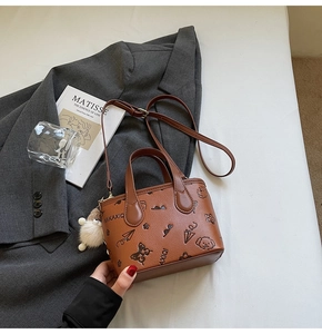 Close-up of brown textured leather bag with cartoon embossing and fuzzy white pom charm