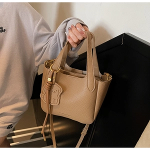 Detail of khaki leather bucket bag with dog charm and gold hardware on grey background
