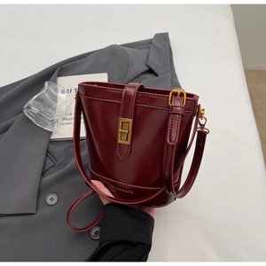 Dettaglio borsa a secchiello bordeaux con chiusura dorata su blazer grigio