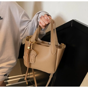 Detail of khaki pebbled leather bucket bag featuring a bear charm and twin handles