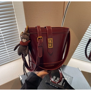 Dettaglio borsa a secchiello rosso scuro con chiusura a scatto dorata e ciondolo a orsetto