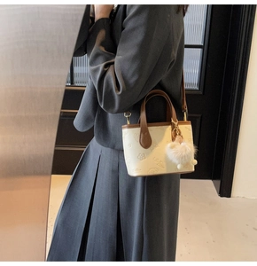 Close-up of embossed patterns on cream leather tote bag with brown handles and plush charm