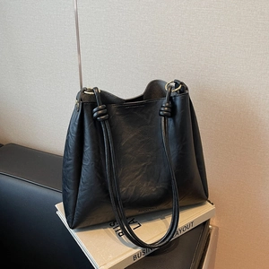 Classic black faux leather tote bag with knotted handles and gold hardware on books