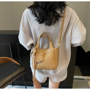 Detail view of khaki pebbled leather bucket bag with a cute dog-shaped charm pendant