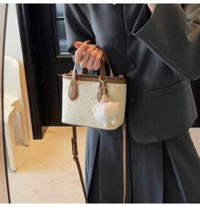 Close-up of embossed patterns and plush charm on cream faux leather bucket bag