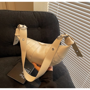 Detailed close-up of cream leather croissant bag featuring metallic ring buckle and stitching