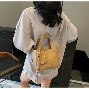 Close-up of camel leather bucket bag with lychee texture and cute bear pendant charm