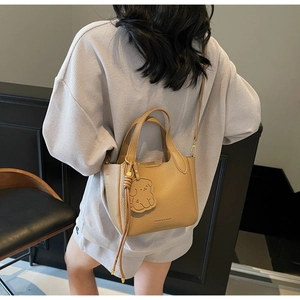 Detail of tan lychee grain leather bucket bag featuring a cute puppy charm and dual handles