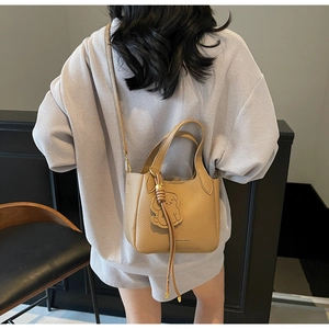 Close-up of khaki pebbled leather bucket bag with bear charm and tassel details