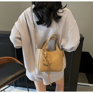 Rear view of a camel leather bucket bag with bear charm and adjustable shoulder strap