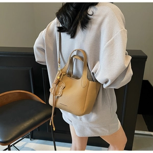 Detail of khaki pebbled leather bucket bag featuring cute dog charm and shoulder strap