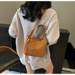 Caramel bucket bag detail showing lychee texture, dog charm and model outfit matching