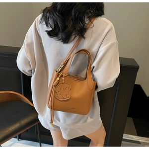 Brown bucket bag featuring pebbled leather texture and a cute dog-shaped charm detail