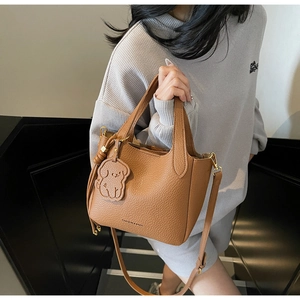 Detailed shot of brown lychee grain bucket bag with a cute dog charm and crossbody strap