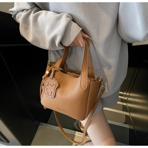 Close-up of caramel brown pebble leather bucket bag with cute dog charm and logo detail