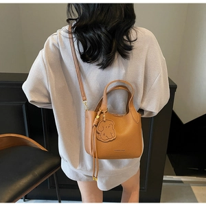 Brown litchi leather bucket bag shown on shoulder with cute dog charm and logo detail