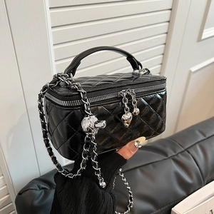 Chic black quilted box bag with silver chain strap and heart charm in a modern room