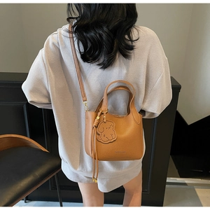 Brown lychee leather tote bag with a dog charm and adjustable strap worn by a model