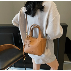 Detail of caramel leather bucket bag with dog pendant worn over a plaid outfit
