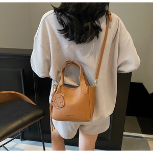 Detail view of brown textured leather bucket bag with dog charm and fashion logo