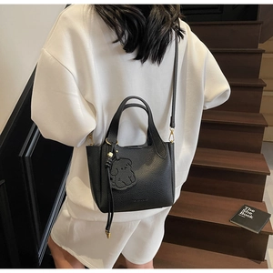 Detail of black pebbled leather bucket bag featuring round handles and a puppy charm
