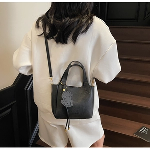 Close-up of black lychee leather bucket bag with cute puppy charm and detachable strap