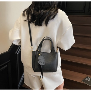 Close-up of black lychee grain leather bucket bag with gold hardware and dog charm